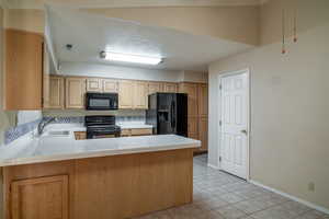 Kitchen with black appliances, a sink, tile counters, light brown cabinets, and light tile patterned floors