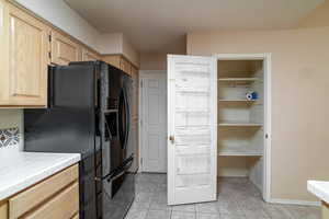 Kitchen featuring tile countertops, light brown cabinetry, black fridge with ice dispenser, light tile patterned floors, and baseboards