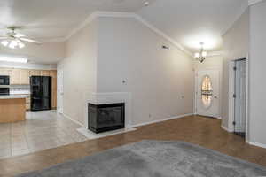 Unfurnished living room with vaulted ceiling, ceiling fan, light tile patterned flooring, a chandelier, and a multi sided fireplace
