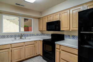 Kitchen featuring black appliances, a sink, tasteful backsplash, light tile patterned floors, and light brown cabinetry