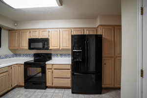 Kitchen featuring black appliances, tile countertops, light brown cabinets, and light tile patterned floors