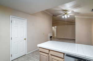 Kitchen with stainless steel dishwasher, ceiling fan, tile countertops, baseboards, and light brown cabinets