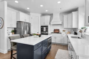 Kitchen featuring blue cabinets, stainless steel appliances, white cabinetry, a kitchen bar, and light wood-style floors