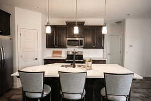 Kitchen featuring appliances with stainless steel finishes, backsplash, a center island with sink, light countertops, and recessed lighting