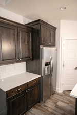 Kitchen with stainless steel fridge, wood finished floors, dark brown cabinetry, light countertops, and a textured ceiling