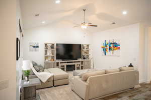 Living area with a ceiling fan, lofted ceiling, a glass covered fireplace, recessed lighting, and wood finished floors