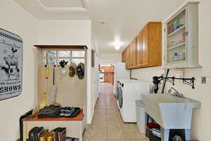 Washroom with cabinet space, light tile patterned floors, and washer and clothes dryer