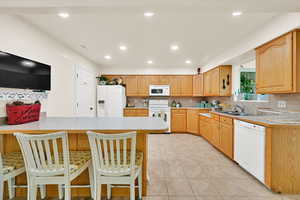 Kitchen featuring white appliances, light countertops, a breakfast bar, tasteful backsplash, and a peninsula