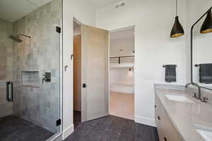 Bathroom featuring a shower stall, double vanity, tile patterned floors, and baseboards