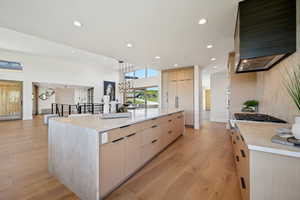 Kitchen featuring modern cabinets, wall chimney range hood, light brown cabinets, light wood-type flooring, and recessed lighting