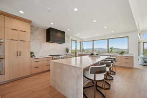 Kitchen featuring modern cabinets, light brown cabinetry, wall chimney exhaust hood, and recessed lighting