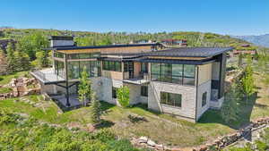 Rear view of property featuring a standing seam roof, stone siding, metal roof, a balcony, and a sunroom