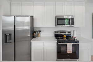 Kitchen with stainless steel appliances, white cabinetry, and light countertops