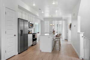 Kitchen featuring appliances with stainless steel finishes, white cabinets, an island with sink, light wood-style floors, and a kitchen breakfast bar
