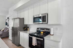Kitchen with appliances with stainless steel finishes, light countertops, light wood-style floors, white cabinetry, and open floor plan