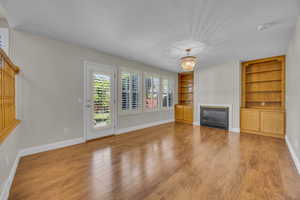 Unfurnished living room with built in shelves, wood finished floors, a glass covered fireplace, and a chandelier