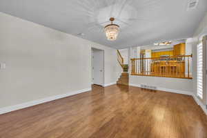 Unfurnished living room with a chandelier, stairs, wood finished floors, and plenty of natural light