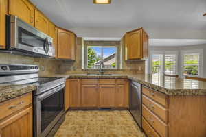 Kitchen featuring stainless steel appliances, a peninsula, decorative backsplash, and brown cabinetry
