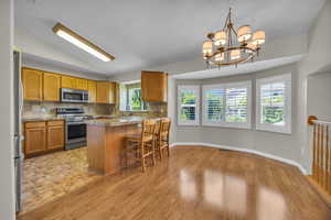 Kitchen with stainless steel appliances, backsplash, a breakfast bar, brown cabinetry, and vaulted ceiling