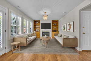 Living room featuring built in features, wood finished floors, a chandelier, and a glass covered fireplace