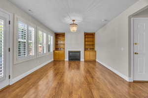 Unfurnished living room with built in shelves, wood finished floors, a glass covered fireplace, and a chandelier