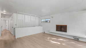 Unfurnished living room with wood finished floors, a fireplace, and brick wall