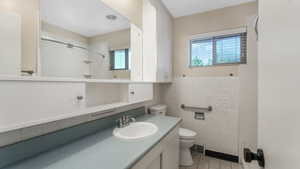 Bathroom with toilet, vanity, tile patterned flooring, tile walls, and a shower