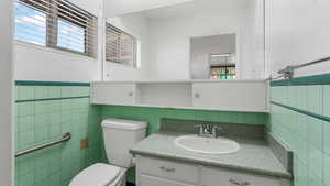 Half bath featuring tile walls, toilet, vanity, and a wainscoted wall