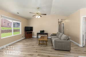 Living room featuring light wood finished floors, ceiling fan, vaulted ceiling, and baseboards