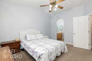 Bedroom featuring light colored carpet, arched walkways, lofted ceiling, baseboards, and connected bathroom