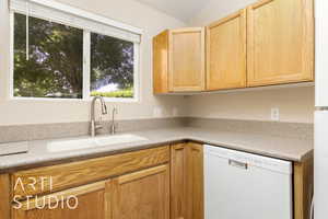 Kitchen featuring white dishwasher, a sink, light countertops, and light brown cabinetry