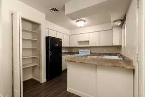 Kitchen featuring freestanding refrigerator, electric stove, a sink, a peninsula, and dark wood-style flooring
