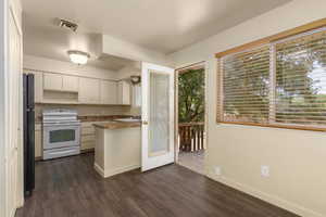 Kitchen with electric range, dark wood-style flooring, white cabinetry, and baseboards