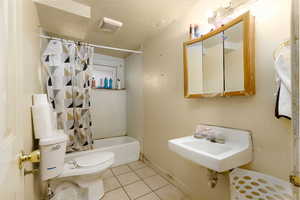 Full bathroom with tile patterned floors, toilet, shower / tub combo with curtain, a sink, and a textured ceiling