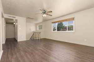 Empty room featuring dark wood finished floors, ceiling fan, and baseboards