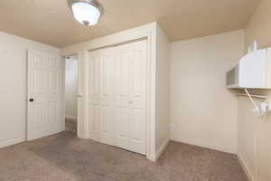 Unfurnished bedroom with a textured ceiling, carpet flooring, a closet, and a wall mounted air conditioner