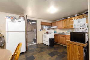 Kitchen featuring white appliances, stone tile flooring, light countertops, brown cabinets, and under cabinet range hood