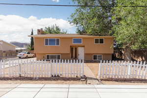 Split foyer home with stucco siding, a fenced front yard, and a chimney