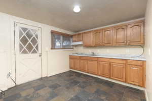 Kitchen with a textured ceiling, light countertops, dark stone finish floors, and brown cabinetry