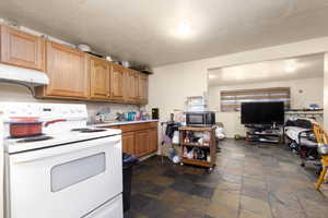 Kitchen featuring white electric range oven, under cabinet range hood, stone tile floors, light countertops, and a textured ceiling