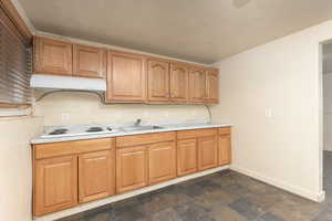 Kitchen with stone tile flooring, light countertops, under cabinet range hood, white electric cooktop, and a textured ceiling