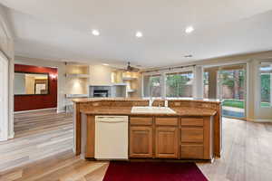 Kitchen with dishwasher, a fireplace, a ceiling fan, light wood-style flooring, and an island with sink