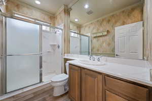 Full bathroom featuring crown molding, vanity, wood finished floors, a shower stall, and wallpapered walls