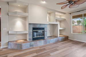 Unfurnished living room featuring wood finished floors, a tiled fireplace, ceiling fan, and recessed lighting