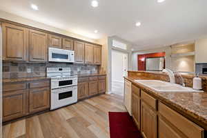 Kitchen with white appliances, light wood-type flooring, decorative backsplash, recessed lighting, and dark stone countertops