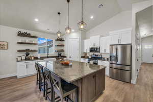 Kitchen with appliances with stainless steel finishes, open shelves, a center island, light wood-style floors, and recessed lighting