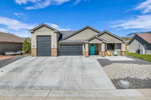 View of front of home with stone siding, a garage, covered porch, and concrete driveway