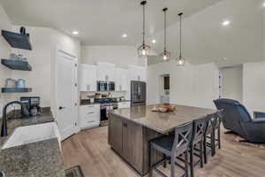 Kitchen featuring appliances with stainless steel finishes, open floor plan, a breakfast bar, white cabinets, and a center island