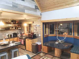 Bar with stainless steel range with gas cooktop, lofted ceiling, light wood-style flooring, black microwave, and wood ceiling