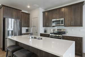 Kitchen with stainless steel appliances, a sink, dark brown cabinets, an island with sink, and light wood-style flooring